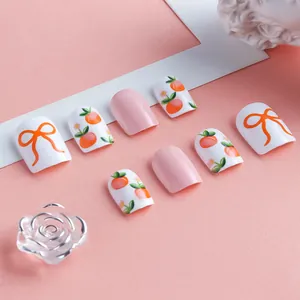 Detail of short square press-on nails with peach patterns and orange bow designs
