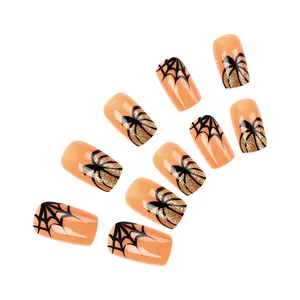 Close-up of glossy short square press-on nails with spider web and glittery pumpkin designs