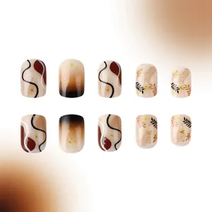 Detail of short round brown press-on nails with leaf patterns and gold foil glitter