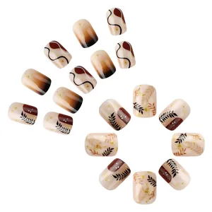 Short glossy press-on nails in mocha brown and cream with leaf patterns and gold foil