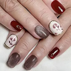 Close-up of deep red glossy nails with rose floral patterns and sparkling glitter finish