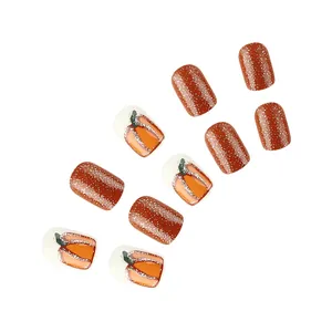 Detail of glittery orange and white press-on nails with cute pumpkin art for Halloween