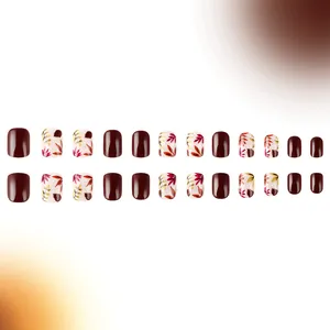 Detalle de uñas postizas cortas cuadradas en color granate con diseños de hojas de otoño
