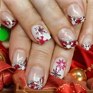 Détail de faux ongles carrés courts avec dégradé de Noël rouge et motifs flocons d'argent