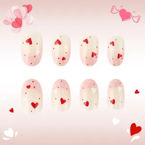 Dettaglio di unghie finte French rosa con motivi a cuore rosso e accenti glitterati