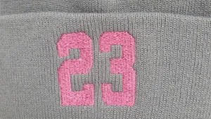 Dettaglio ravvicinato del berretto grigio a maglia con ricamo rosa del numero 23 sul fronte