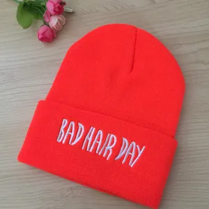 Gros plan sur la broderie blanche BAD HAIR DAY d'un bonnet en maille orange fluo