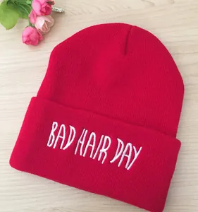 Gros plan de la broderie blanche BAD HAIR DAY sur un bonnet en tricot rouge sur bois