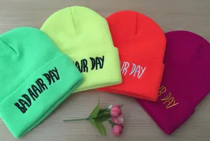 Vue à plat de quatre bonnets en tricot colorés avec broderie Bad Hair Day sur table en bois