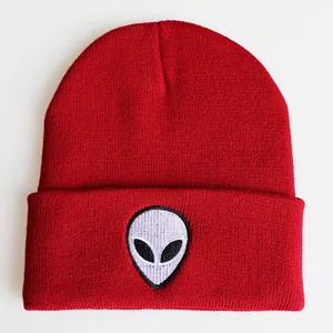 Detail einer roten Rippstrickmütze mit weißem Alien-Kopf-Stickaufnäher