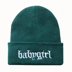 Detail der weißen Babygirl-Stickerei auf dunkelgrüner Strickmütze für Winter