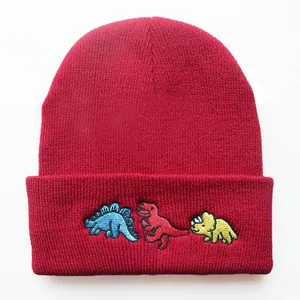 Detail von drei Dinosaurier-Stickereien auf einer roten gerippten Strickmütze