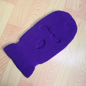 Detalle de un pasamontañas de punto morado con 3 agujeros sobre una superficie de madera
