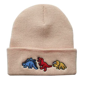 Detailansicht der drei Dinosaurier-Stickereien auf der beigen Strickmütze