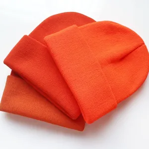 Drei orangefarbene Strickmützen mit Rippenmuster und breitem Umschlag auf weißem Grund