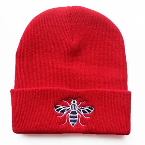 Classic red knitted beanie hat featuring a detailed bee embroidery on the front cuff