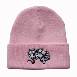 Close-up of pink knit beanie featuring detailed cartoon dragon embroidery on the cuff