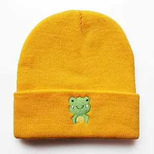 Nahaufnahme der grünen Frosch-Stickerei auf einer leuchtend gelben Strickmütze für Winter