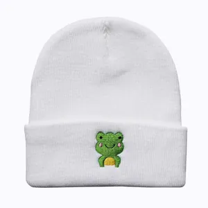 Detail der süßen grünen Frosch-Stickerei auf einer weißen Strickmütze für den Winter