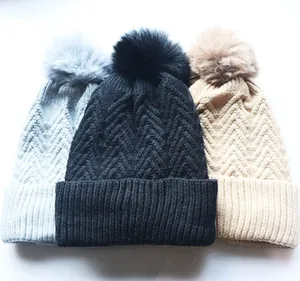 Detail von Strickmützen mit flauschigen Bommeln in den Farben Grau, Schwarz und Beige