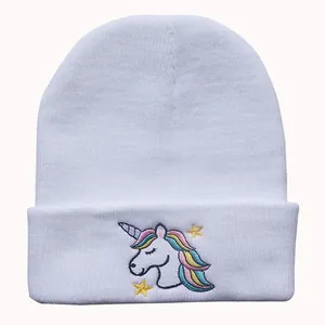 Detailansicht einer weißen Strickmütze mit bunter Einhorn-Stickerei und gelben Sternen
