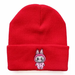 Detailed close-up of red knitted beanie featuring cartoon monster embroidery and texture