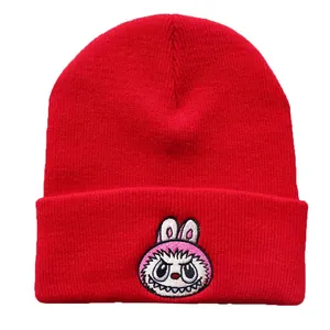 Detailed view of red ribbed knit beanie with pink cartoon embroidery on the folded cuff