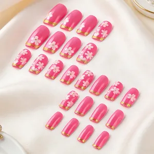Détail de 24 faux ongles roses avec fleurs blanches et bords dorés pailletés