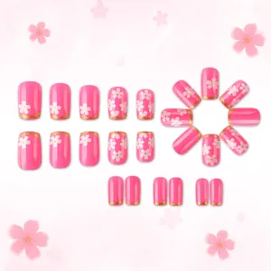Détail de faux ongles roses avec motifs cerisiers blancs et pointes French pailletées dorées