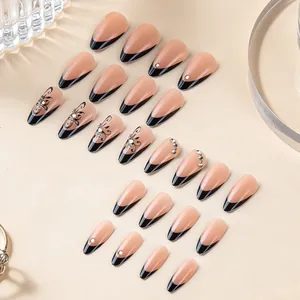 Detail of almond-shaped press-on nails with black French tips, floral patterns and small rhinestones