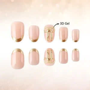 Short round French press-on nails in nude pink with 3D gold gel bows and golden tips