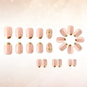 Detail of pink press-on nails with metallic gold French tips and 3D bow accents