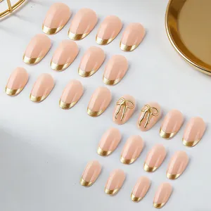 Detail of short round French press-on nails with nude pink base and 3D gold bow accents