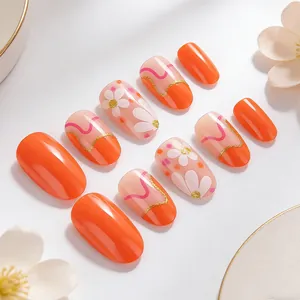 Short oval press-on nails featuring orange floral patterns and golden glitter accents