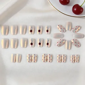 Short pearl white press-on nails with red cherry and polka dot designs on silk background