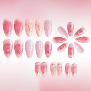 Detailed flat lay of pink gradient almond press-on nails with gold lines and rhinestones