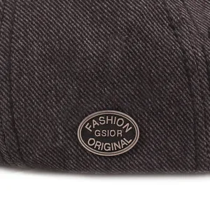 Λεπτομέρεια macro από σκούρο καφέ ύφασμα twill με μεταλλικό λογότυπο στο καπέλο μπερέ