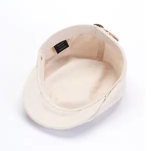 Detailoverzicht van de katoenen baret binnenkant met maatlabel en metalen verstelgesp