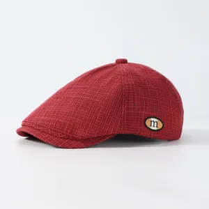 Détail de la casquette plate rouge foncé montrant la texture et l'écusson logo 'm'