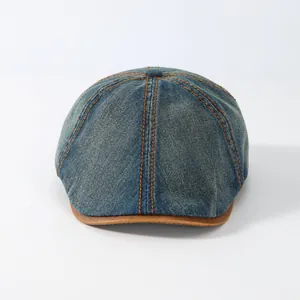 Detail of dark blue washed denim newsboy cap with brown leather brim and orange stitching