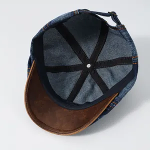 Detail view of denim newsboy cap showing contrast leather brim and adjustable strap