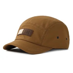 Détail d'une casquette camp beige à cinq panneaux avec écusson bicolore et œillets latéraux