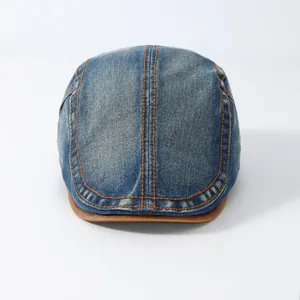 Detail van de blauwe denim platte pet met gele stiksels en bruine lederen klep