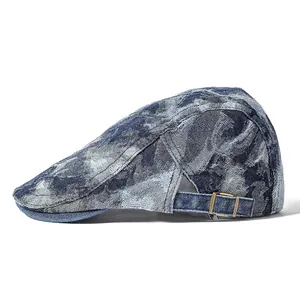 Detail of washed denim newsboy cap showing blue mottled texture and metal buckle