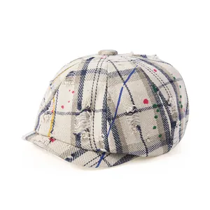 Détail d'une casquette gavroche à carreaux usée avec des taches de peinture et des trous