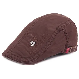 Detail of brown cotton flat cap featuring side embroidery and a metal fashion badge
