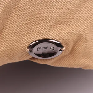 Detailaufnahme der khakifarbenen Stoffstruktur und des ME'S Metall-Logos auf der Mütze