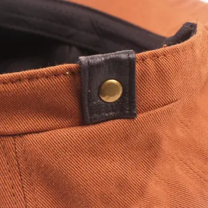 Detail of orange cotton beret featuring black leather trim and bronze metal rivet