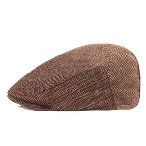 Detail of brown herringbone wool flat cap with a small bronze metal logo tag on the side