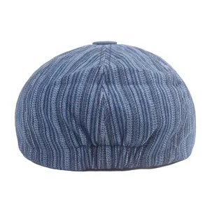 Detailed view of the vertical stripes and top button on this blue denim newsboy cap